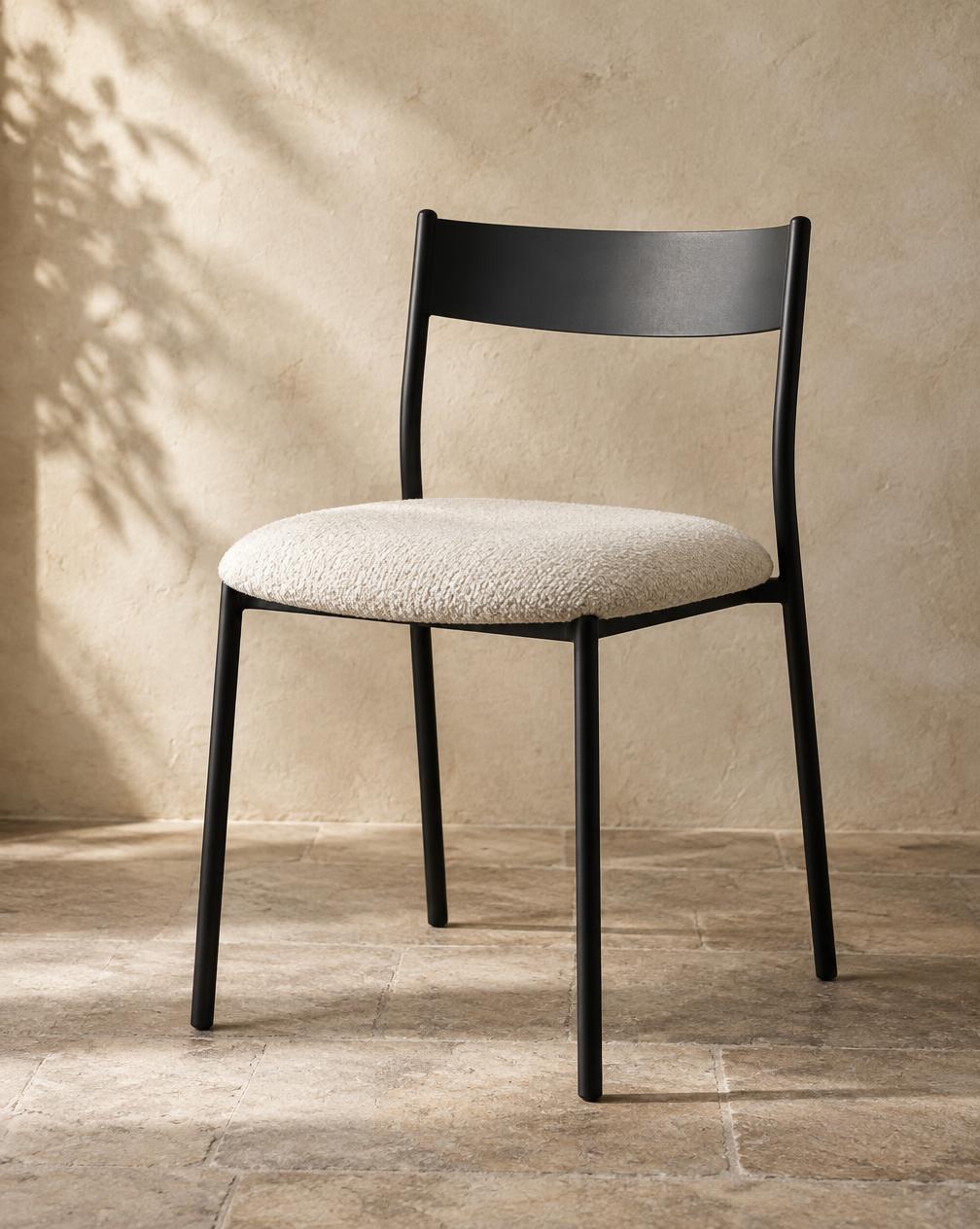 Black steel dining chair with cream bouclé seat against a limestone wall