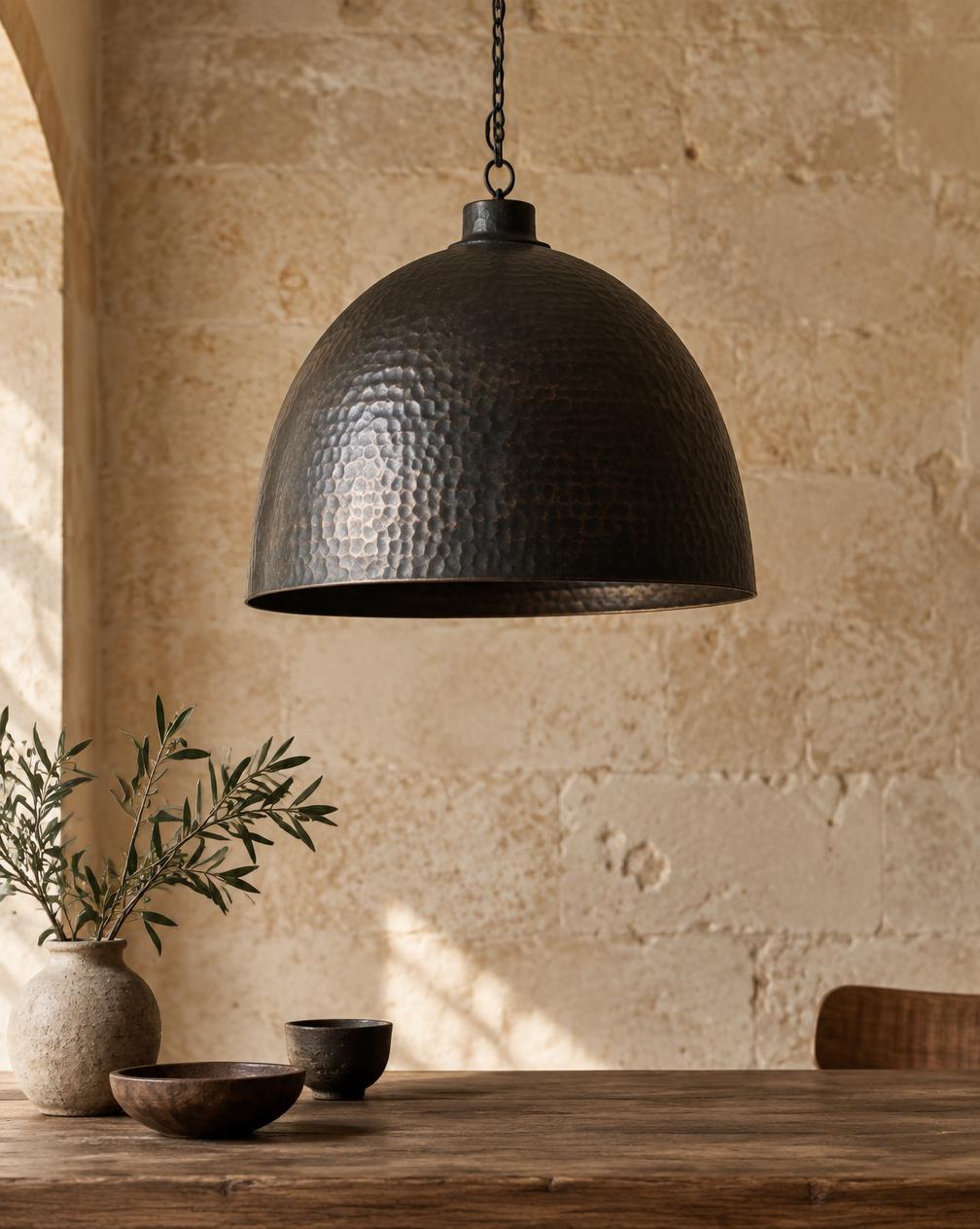 Large hammered blackened metal dome pendant against a limestone wall