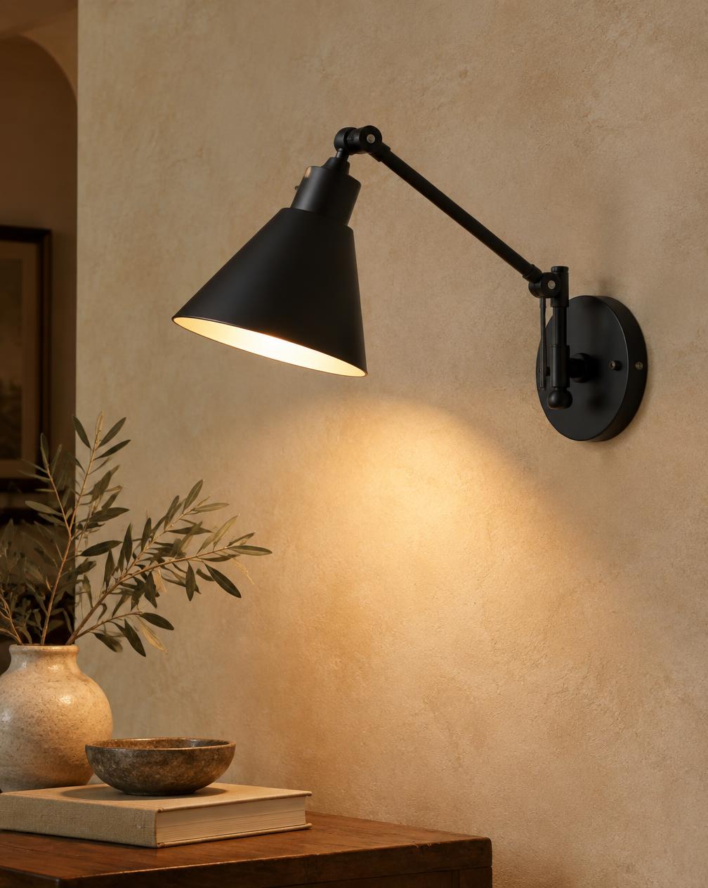 Matte black articulating wall sconce with conical shade on a plaster wall
